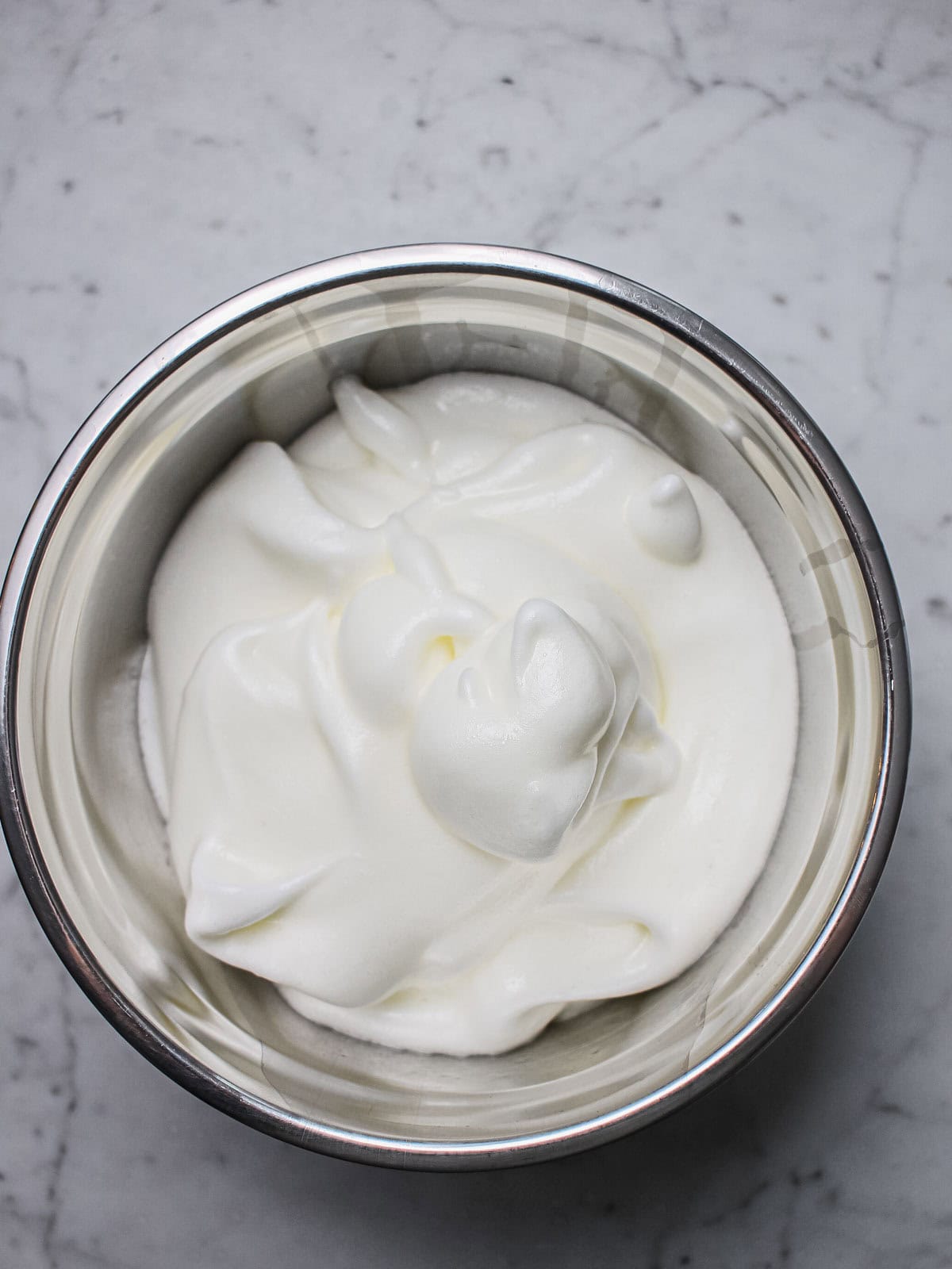 Egg whites beaten to soft peaks with sugar in a mixing bowl.