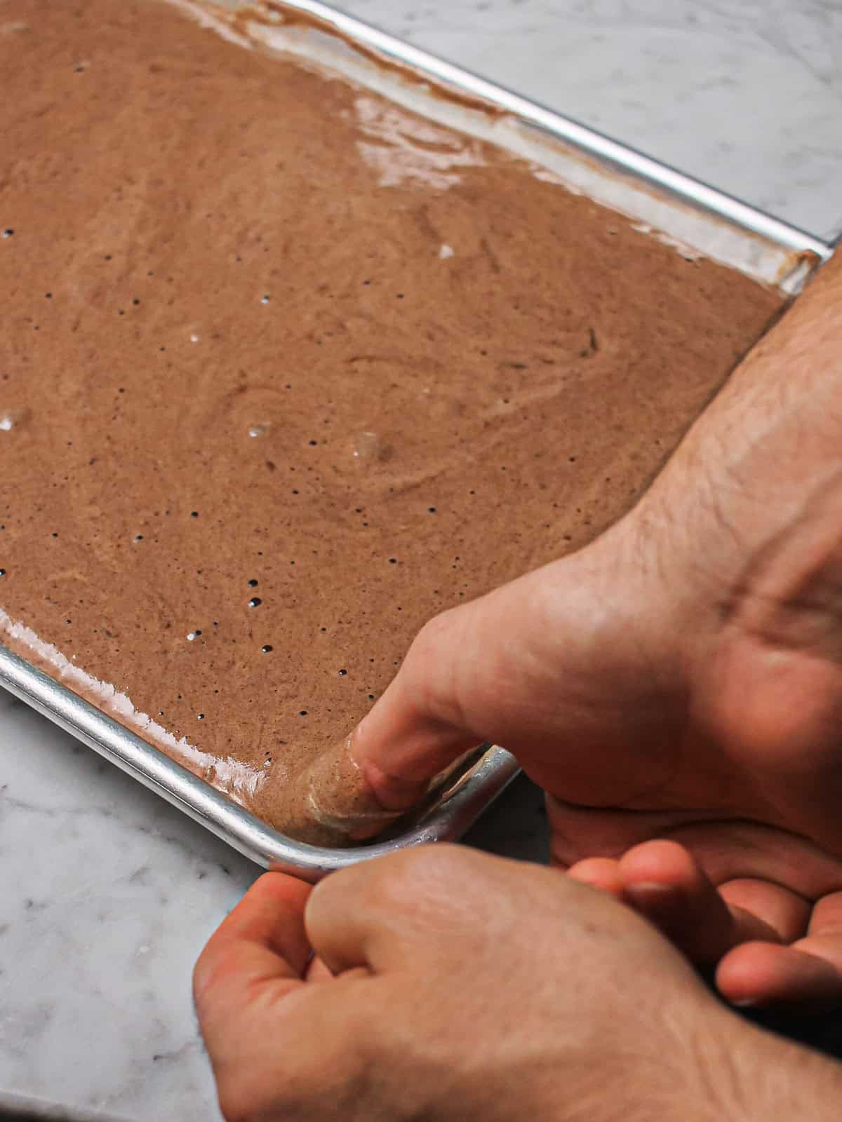 Chocolate sponge batter in a parchment-lined baking sheet.