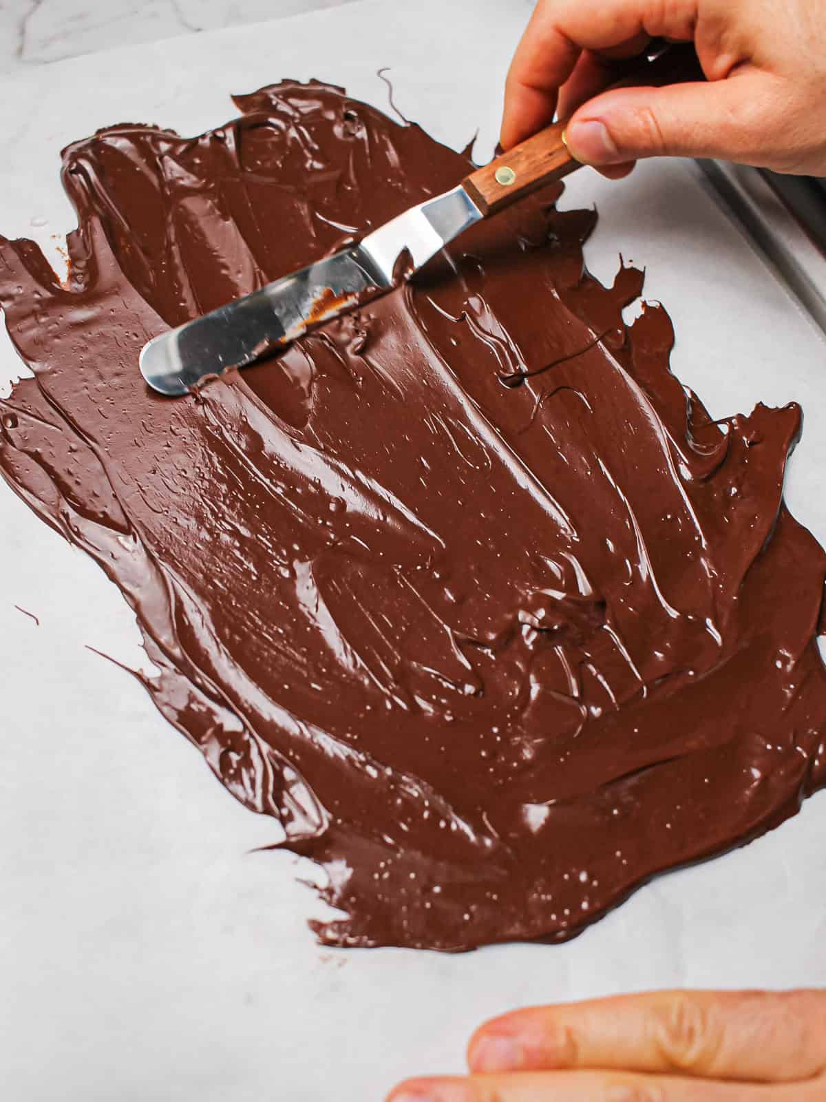 Tempered chocolate spread thinly on parchment with offset spatula.