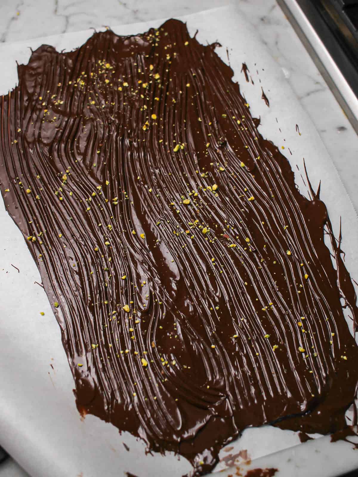 Tempered chocolate spread thinly on parchment with pistachios on top.