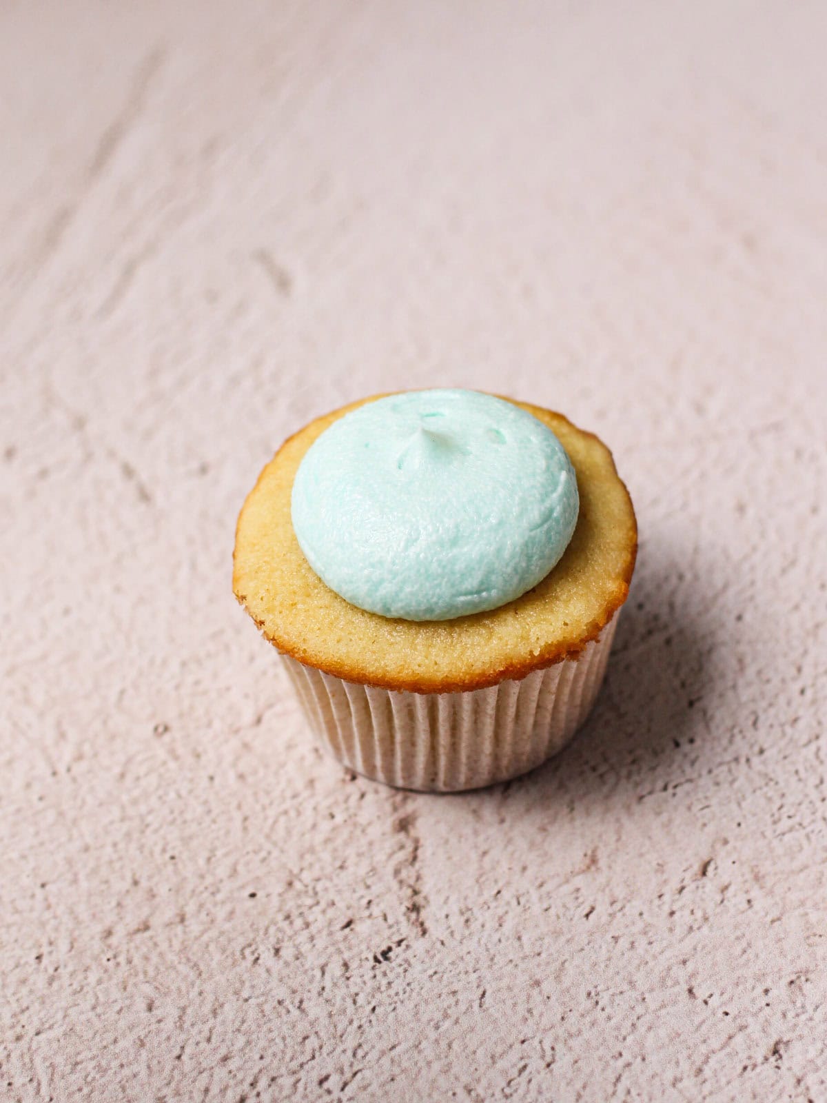Round dollop of blue frosting on a vanilla cupcake.