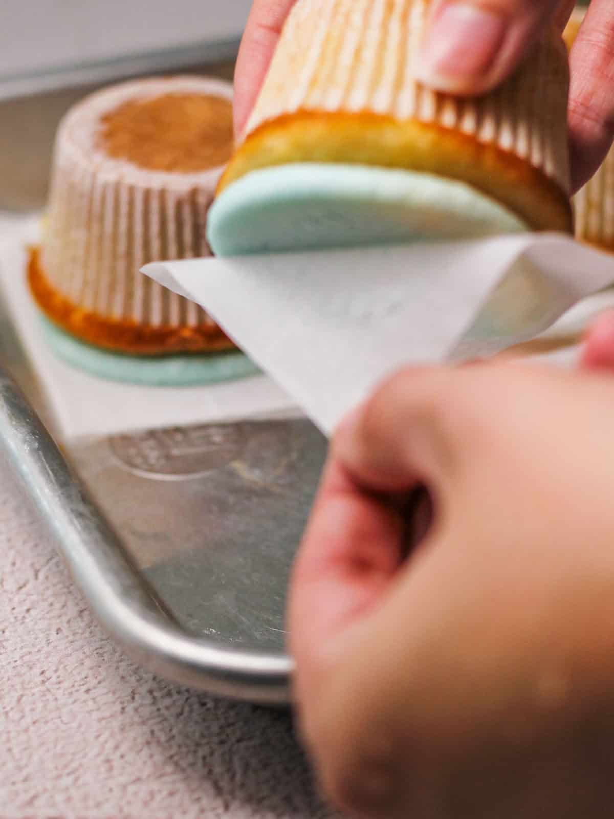 Process shot of removing wax paper from top of cupcake to create the sky background on hot air balloon cupcakes.