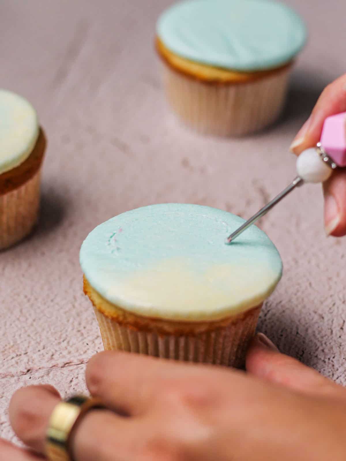 Tracing the outline of a hot air balloon on a frosted vanilla cupcake.