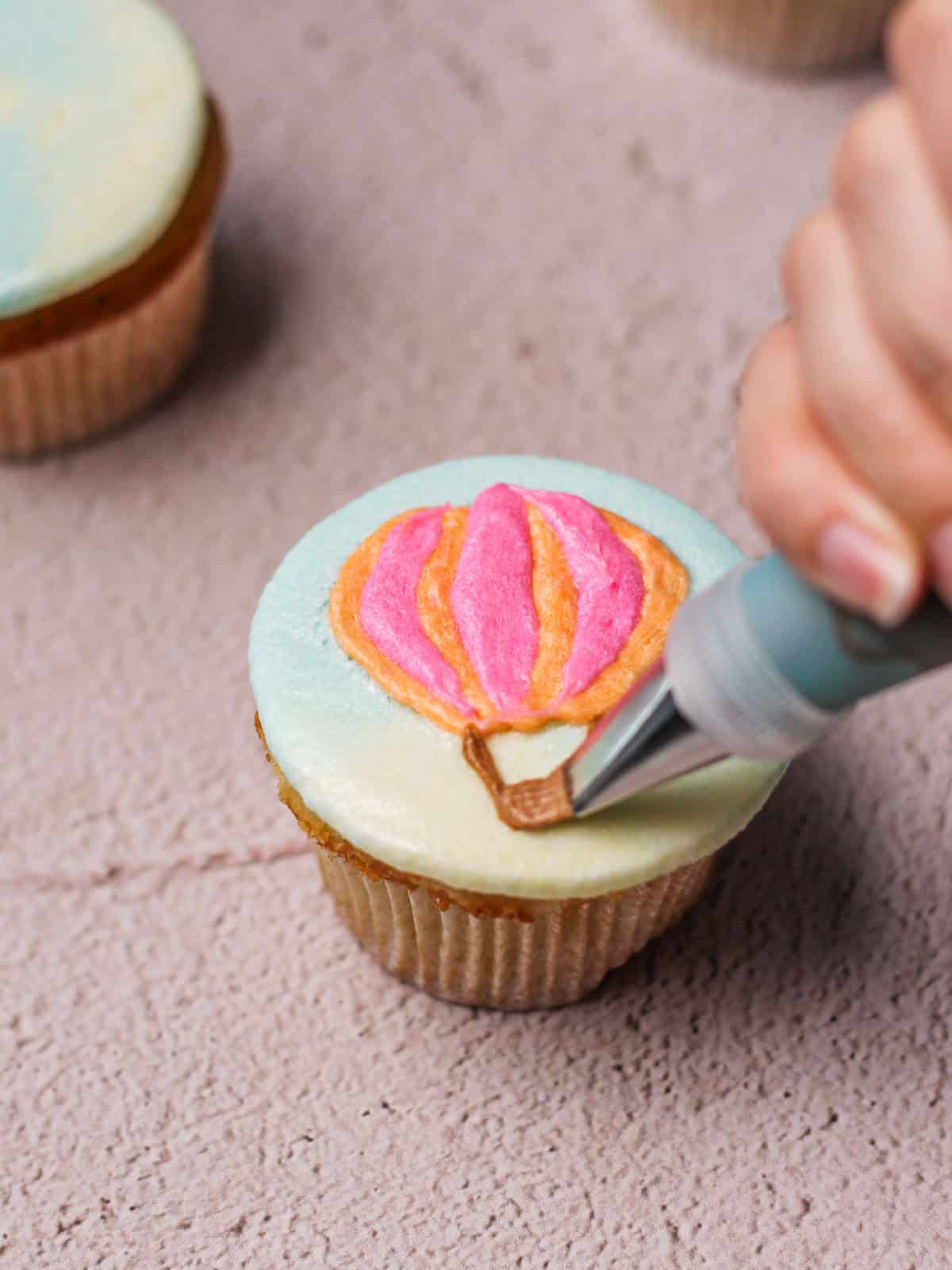 Piping basket onto a cupcake with a hot air balloon design.