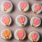 Overhead shot of nine hot air balloon cupcakes, with blue frosting as the background and pink and orange balloons.