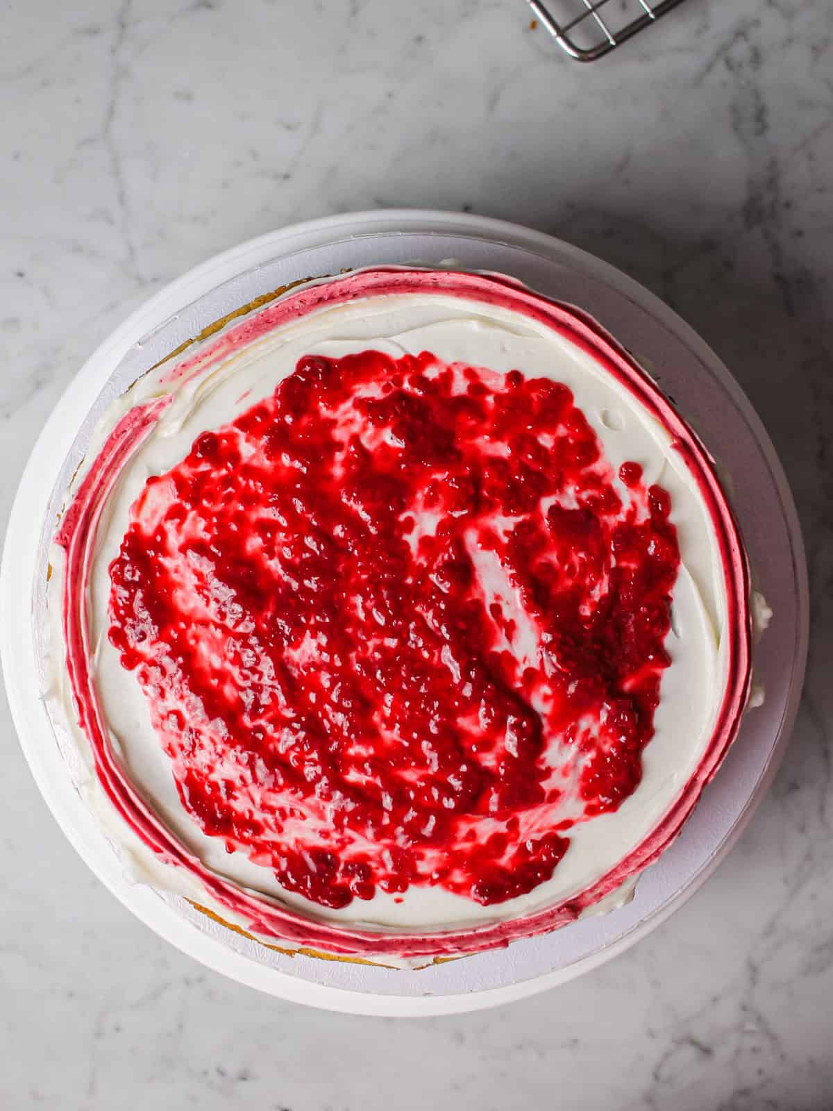 Overhead shot of a cake layer, topped with raspberry filling.