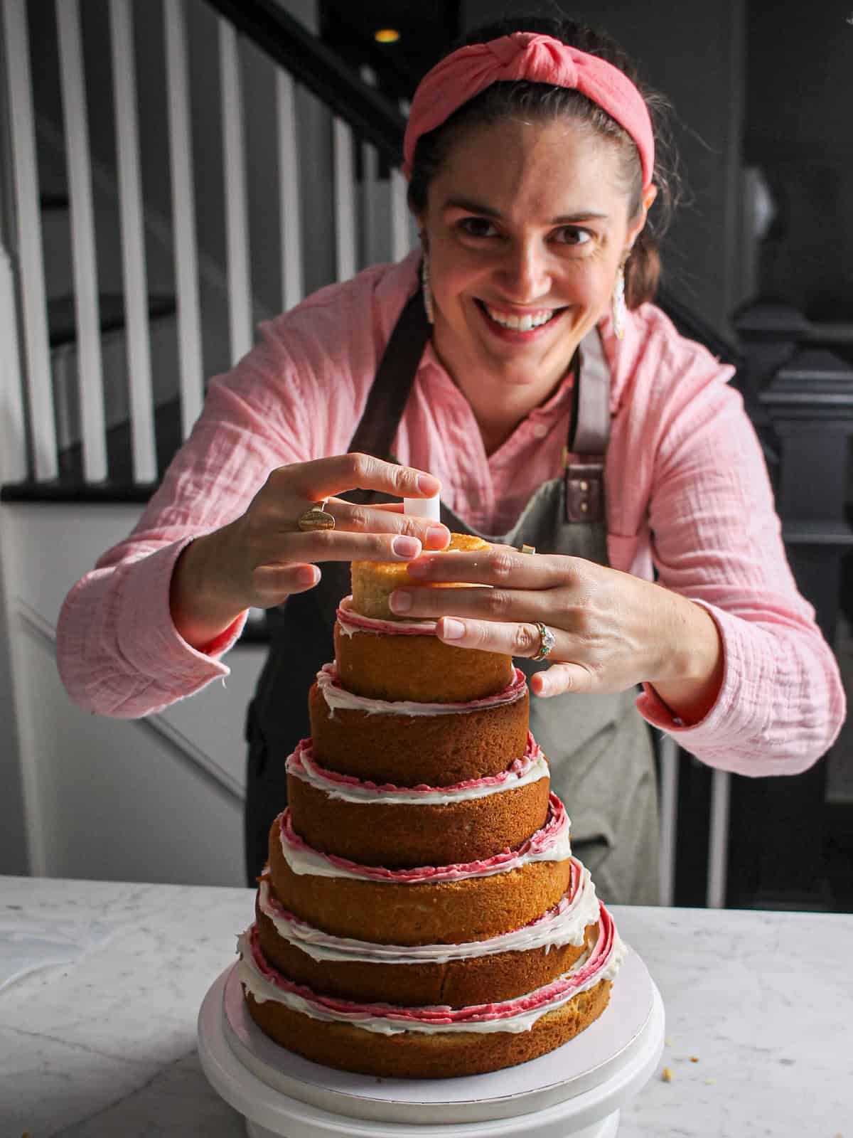 Stacking and doweling layers for a pink 3D Christmas tree cake.