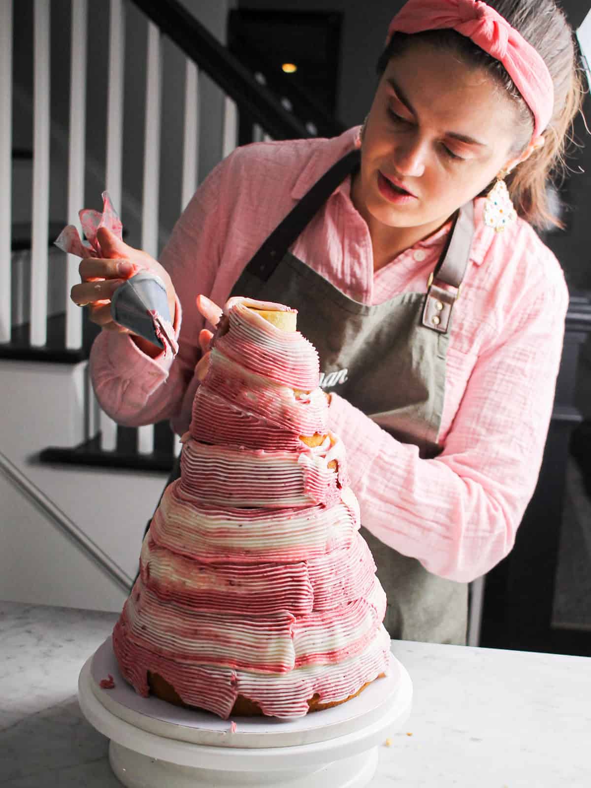 Piping buttercream onto a pink Christmas tree cake.