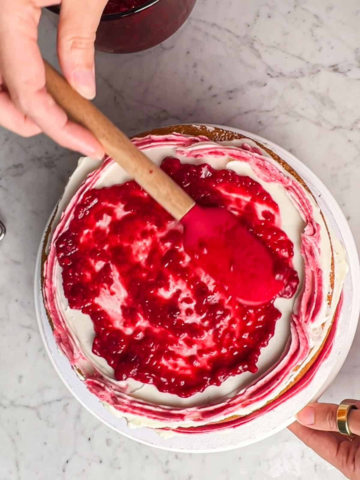 Adding raspberry filling on top of a cake layer.