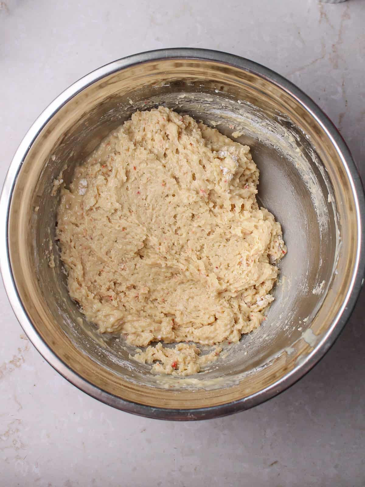 Wet ingredients and dry ingredients combined in a metal mixing bowl to make white chocolate and strawberry muffins.