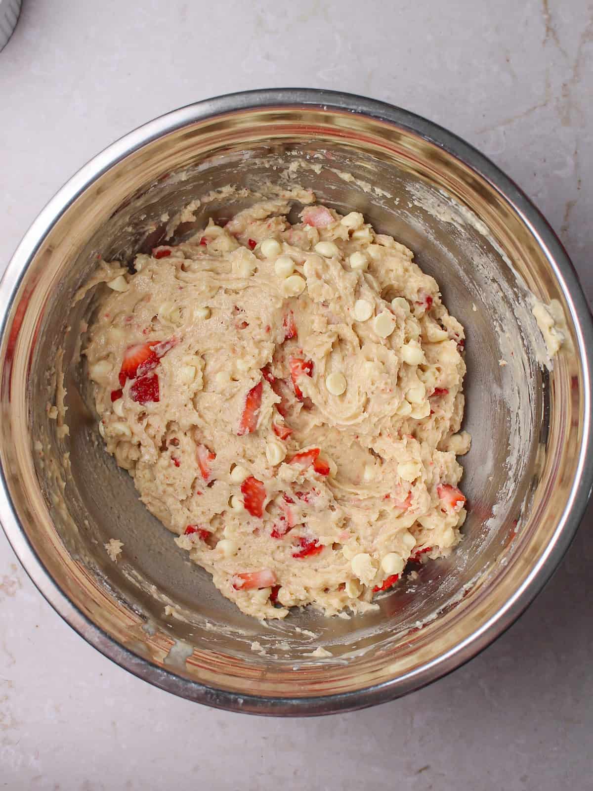 Mixing bowl containing chopped strawberries and white chocolate chips for muffins.