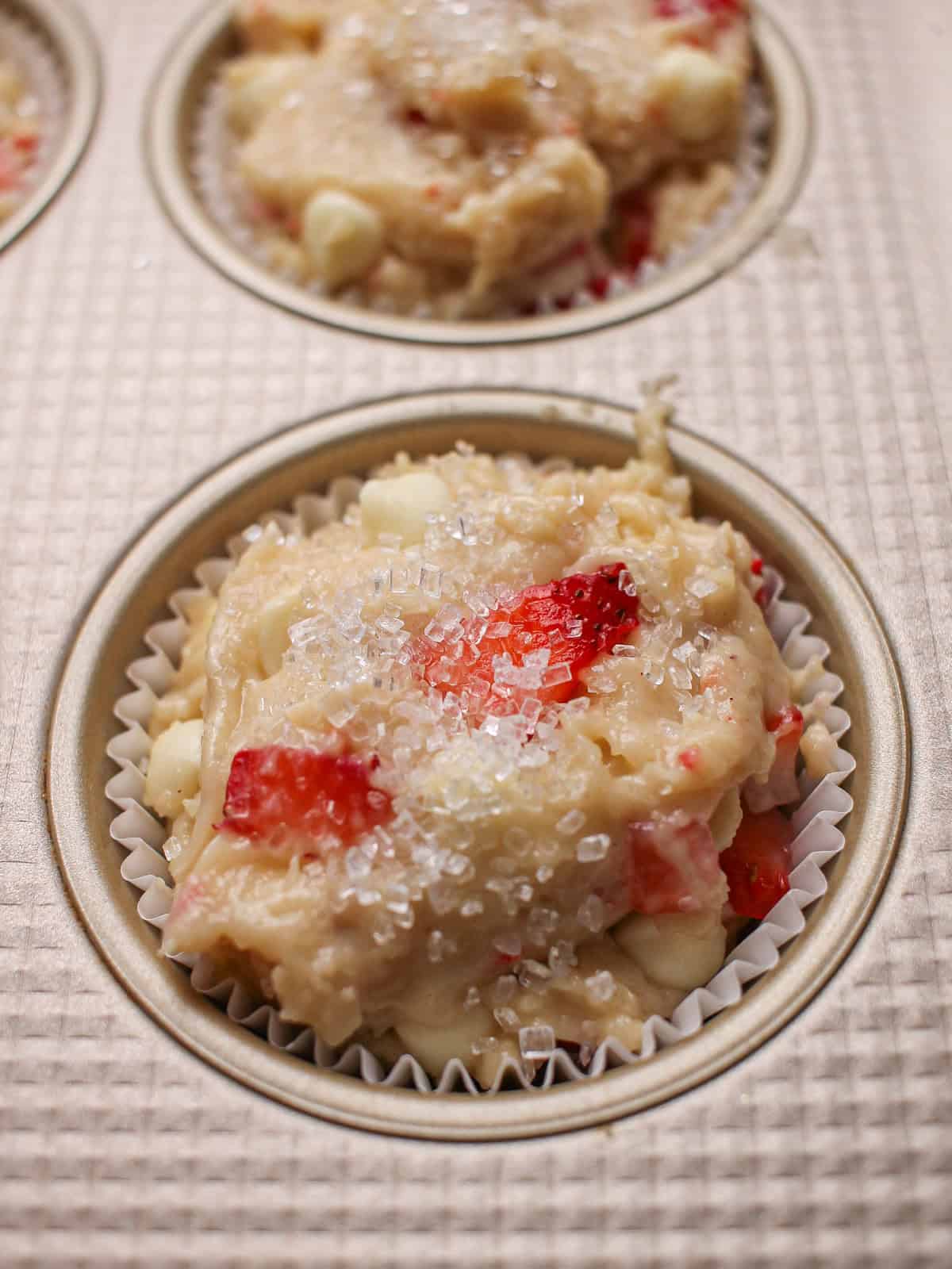 Muffin tin with unbaked white chocolate and strawberry muffins.