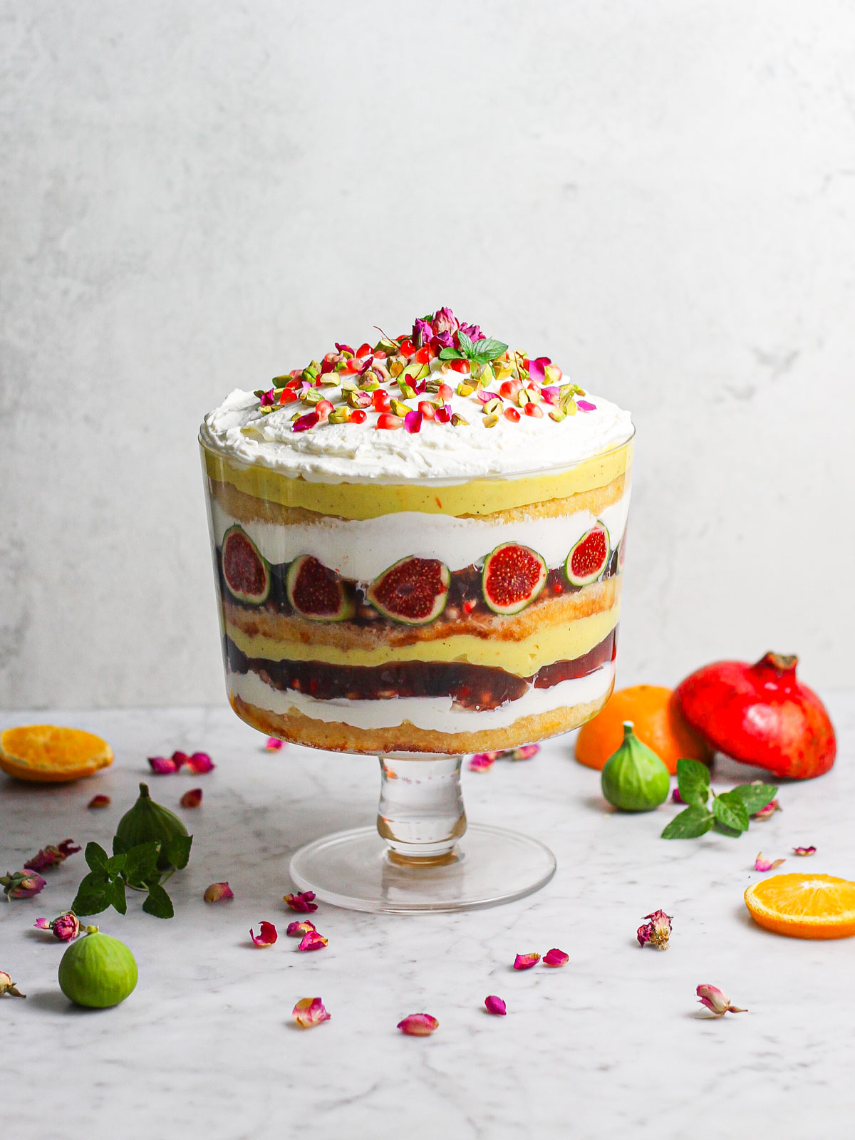 Hero shot of saffron orange trifle with some of the ingredients scattered in the foreground and background (pistachios, rose petals, pomegranates, etc.) 