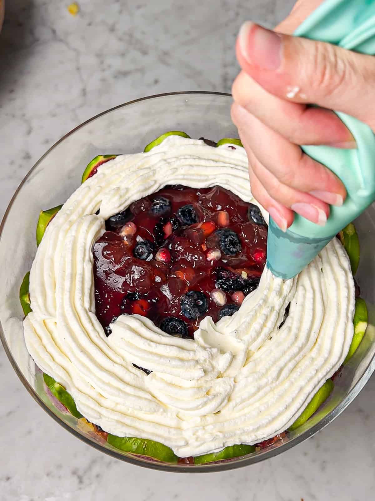 Piping whipped mascarpone cream into trifle dish.
