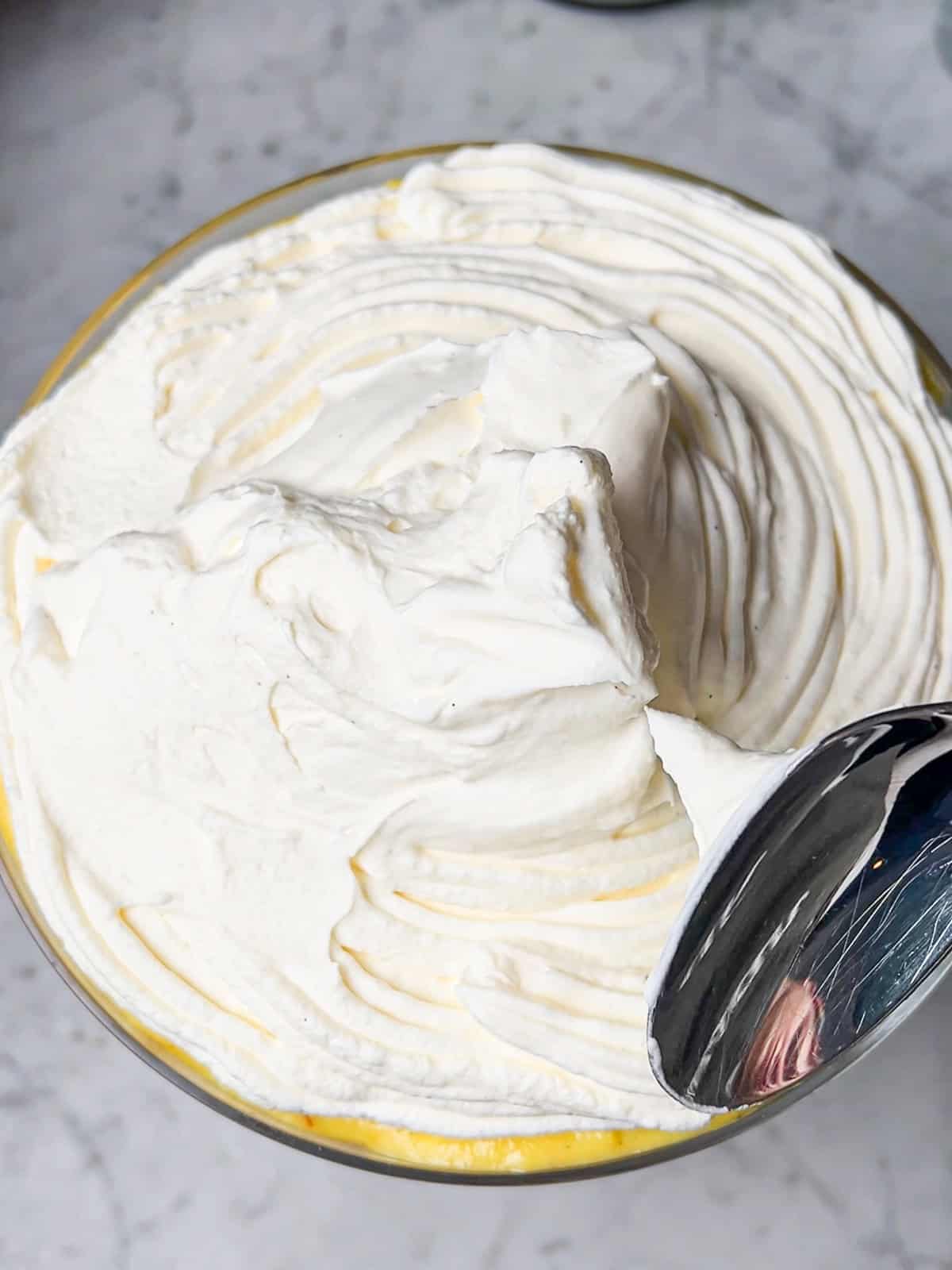 Adding whipped topping to dish containing saffron orange trifle.