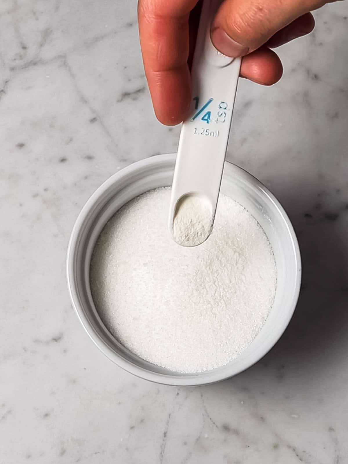 Adding xanthan gum to small container of sugar.