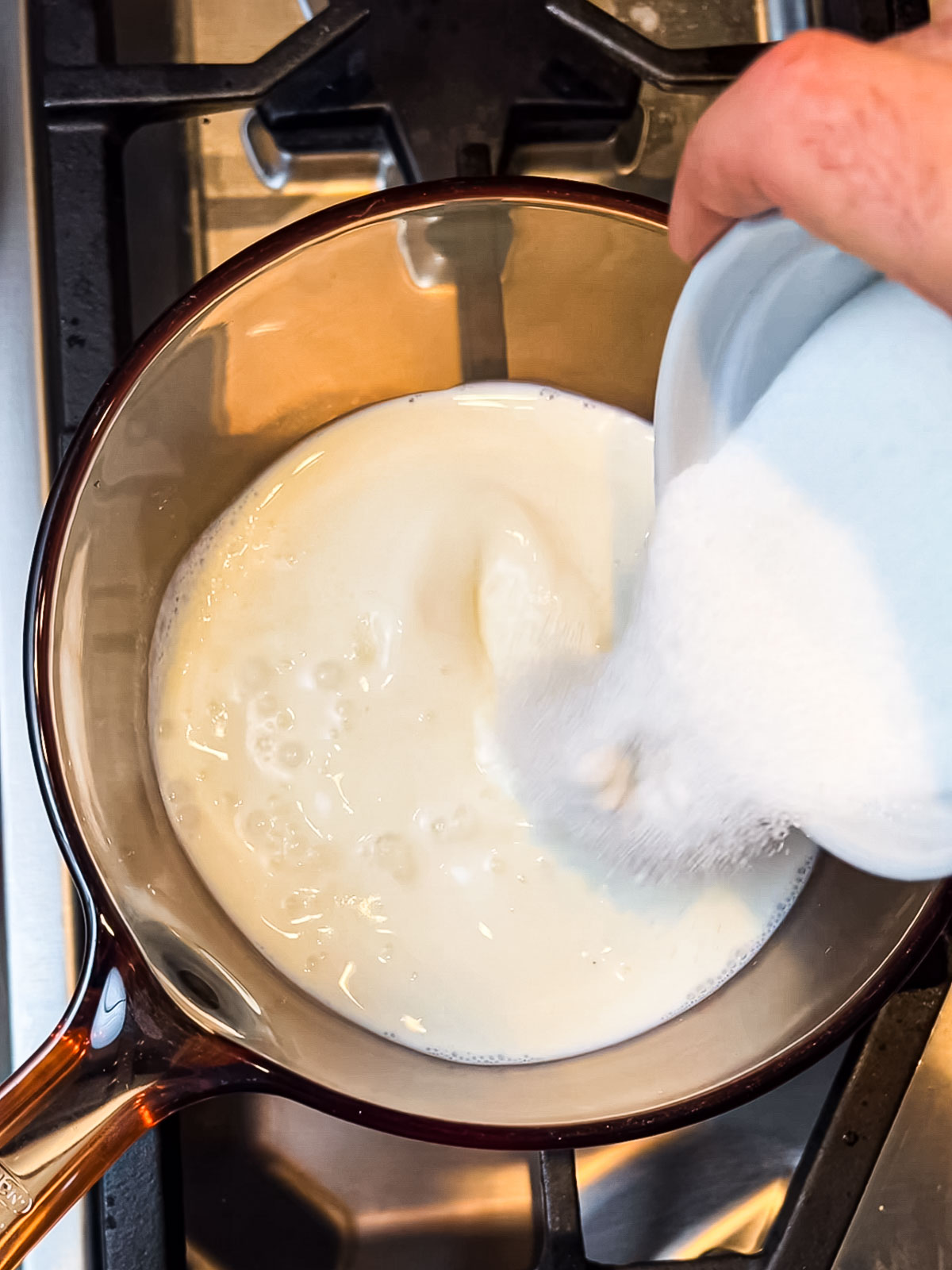 Heating saffron phirni over the stove and adding ingredients to pot.