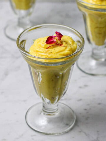 Three glasses of saffron phirni, with a rose petal and saffron thread on top of each one.