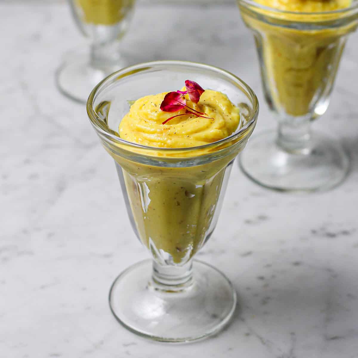 Three glasses of saffron phirni, with a rose petal and saffron thread on top of each one.