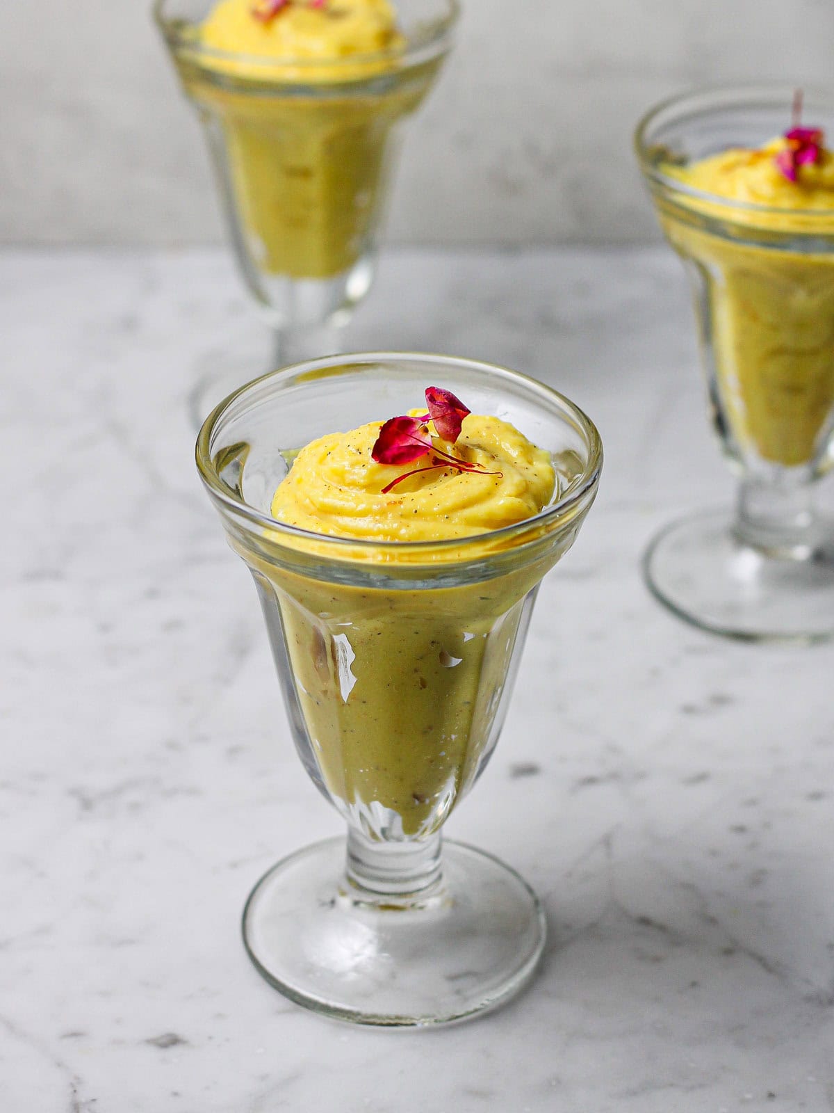 Three glasses of saffron phirni, with a rose petal and saffron thread on top of each one. 