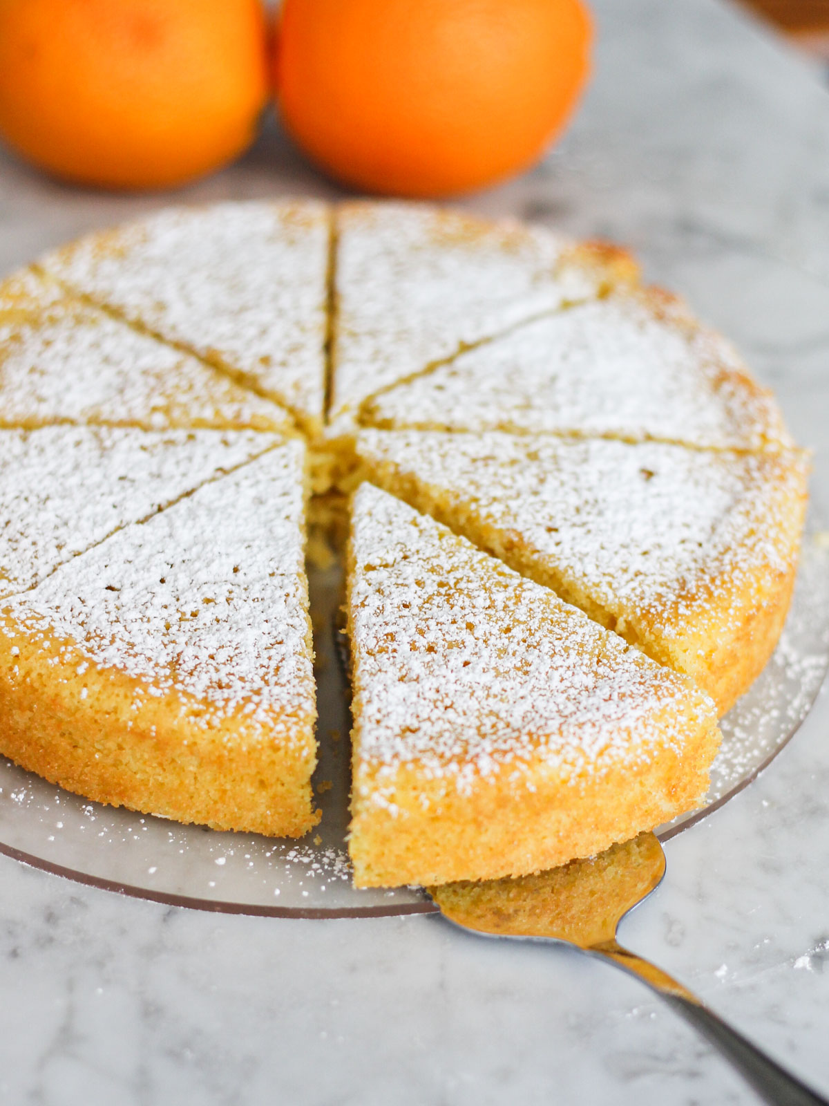 Cake server offset on a cake dish with a slice of Sidi Joon's orange cake on it. Slices are dusted in powdered sugar.