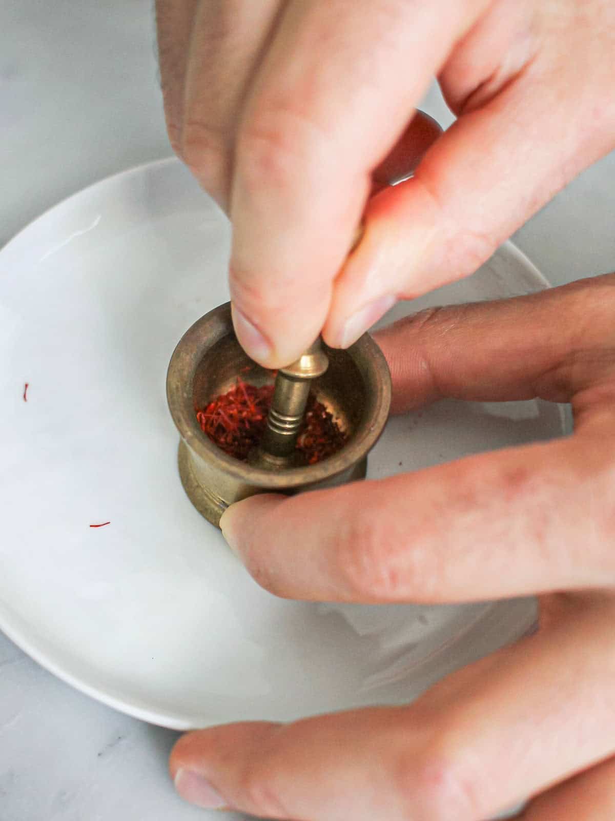 Creating saffron water by grinding saffron threads with a small mortar and pestle.