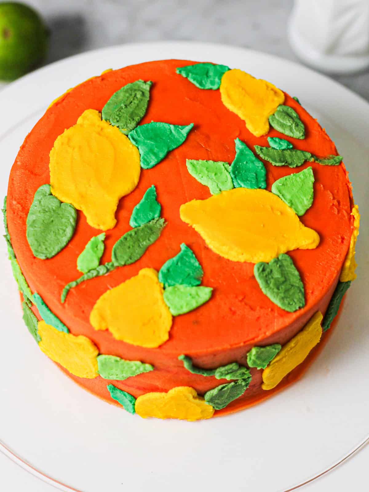 Vibrant orange layered cake decorated with colorful green leaves.