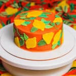 Vibrant orange layered cake decorated with colorful leaves for this buttercream lemon cake tutorial.