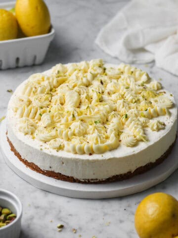 No-bake lemon mascarpone cheesecake topped with whipped white chocolate ganache, sitting on a marbled white and gray countertop.