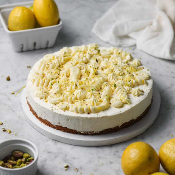 No-bake lemon mascarpone cheesecake topped with whipped white chocolate ganache, sitting on a marbled white and gray countertop.