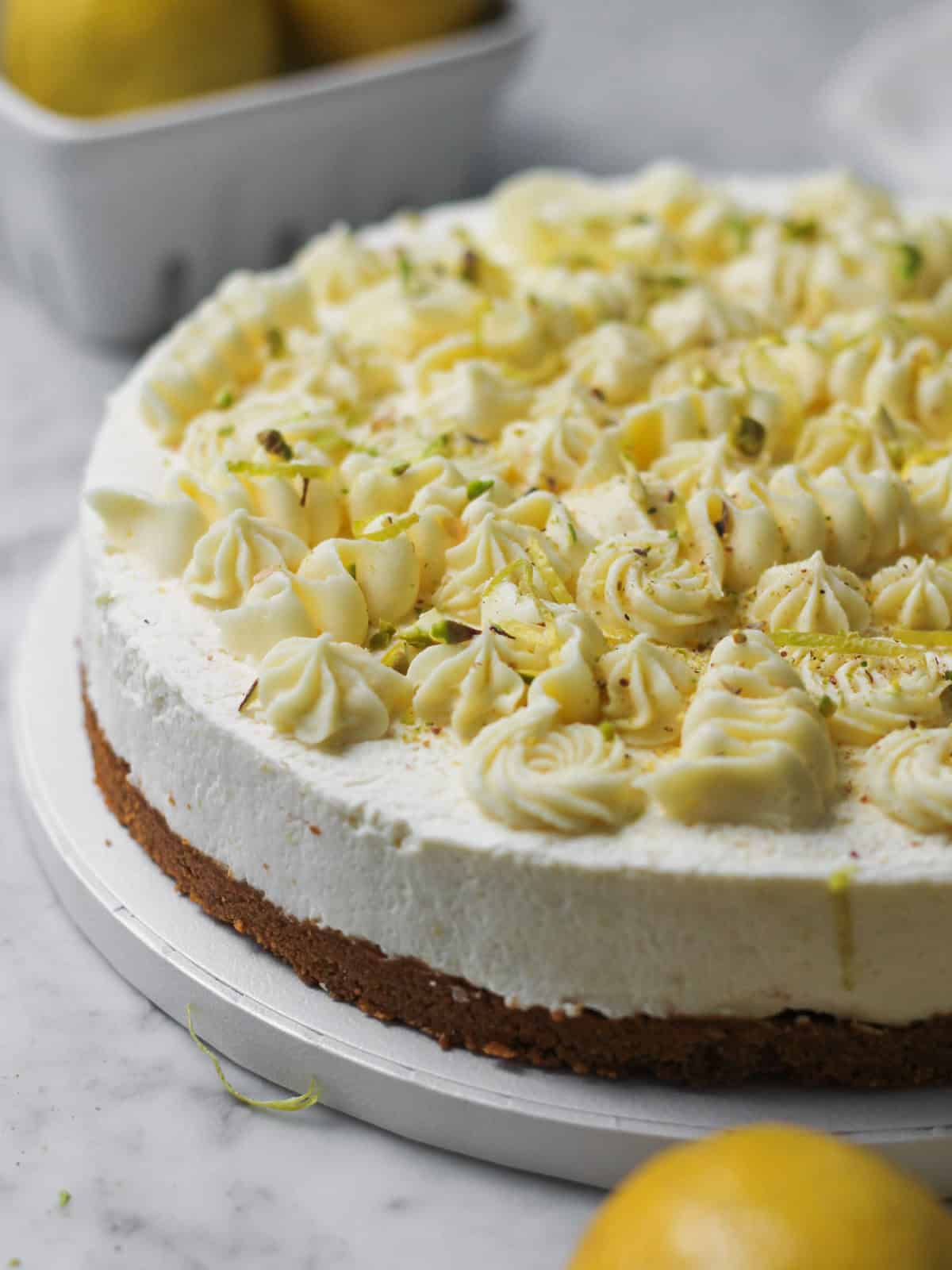 Cheesecake garnished with lemon zest, pistachios, and white chocolate ganache piped on top.