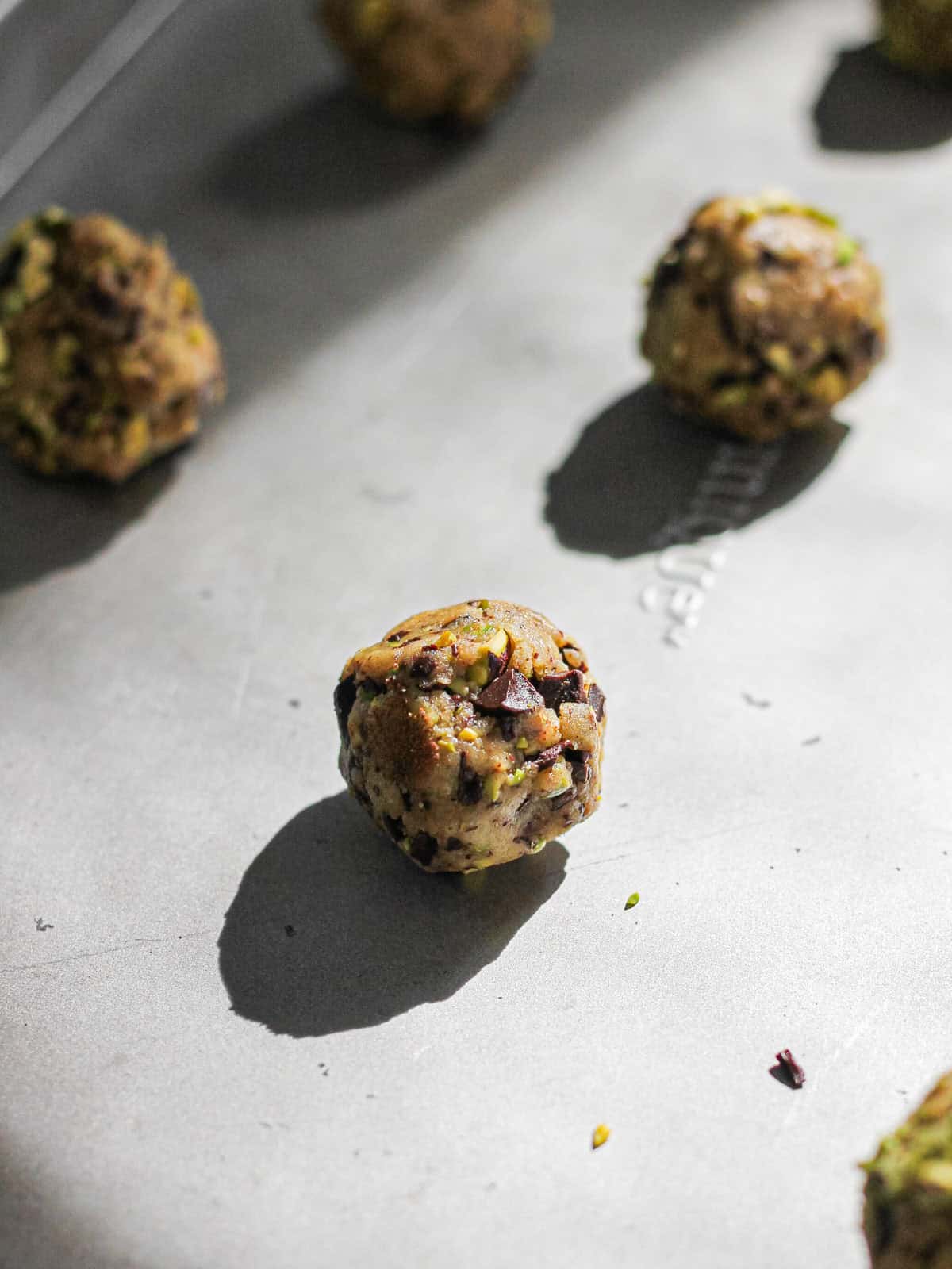 Pistachio dark chocolate cookie dough balls on a baking sheet.