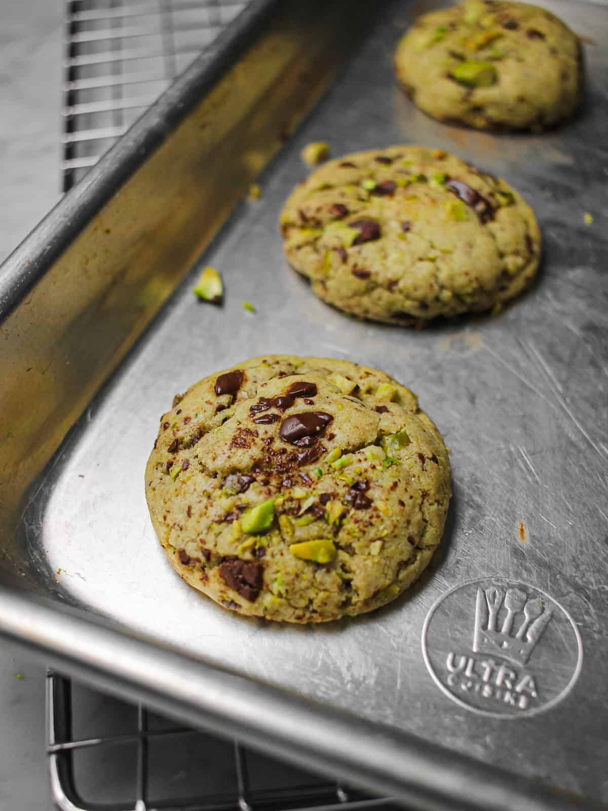 Baked brown butter pistachio cookies with melty chocolate pools, sitting on a cookie sheet.