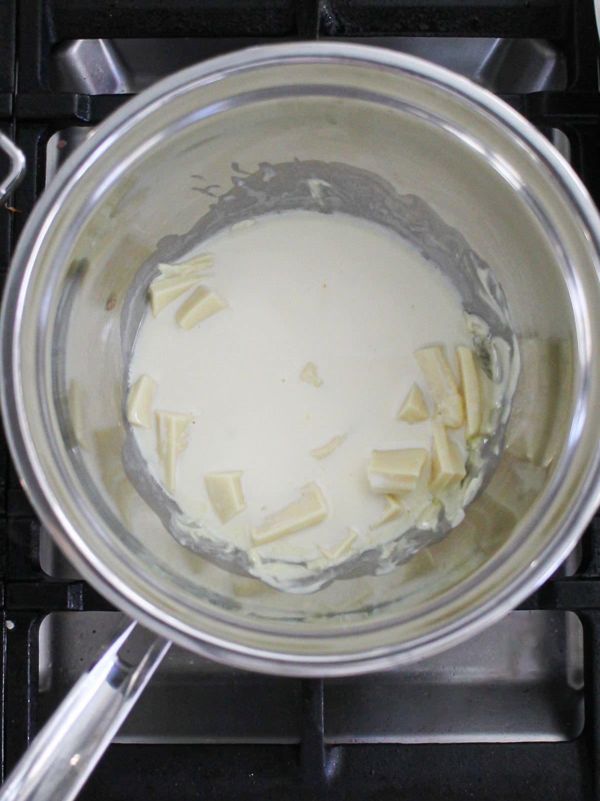 Hot cream poured over chopped white chocolate in a bowl.