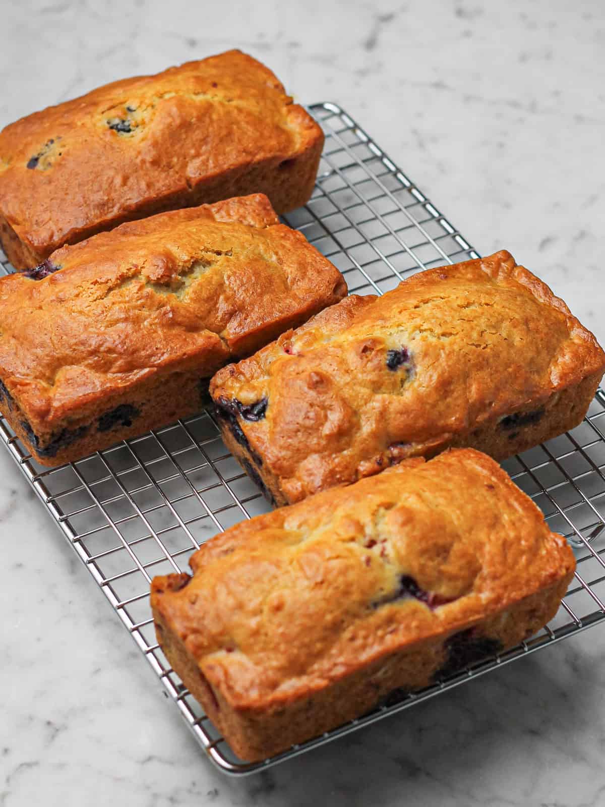 Freshly baked mini mixed berry loaf cakes cooling on a wire rack before glazing.