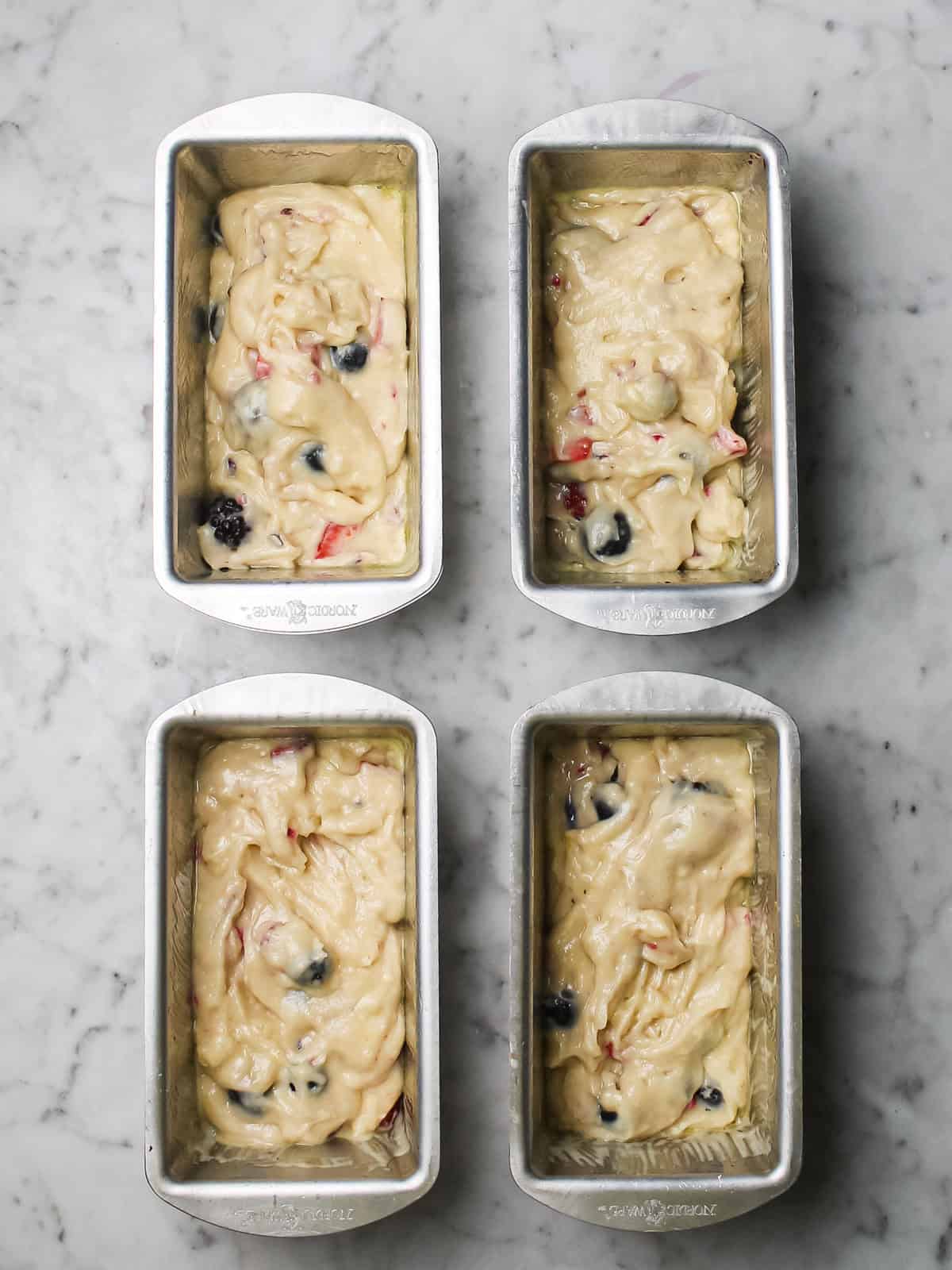 Mixed berry loaf cake batter divided among four greased mini loaf pans.