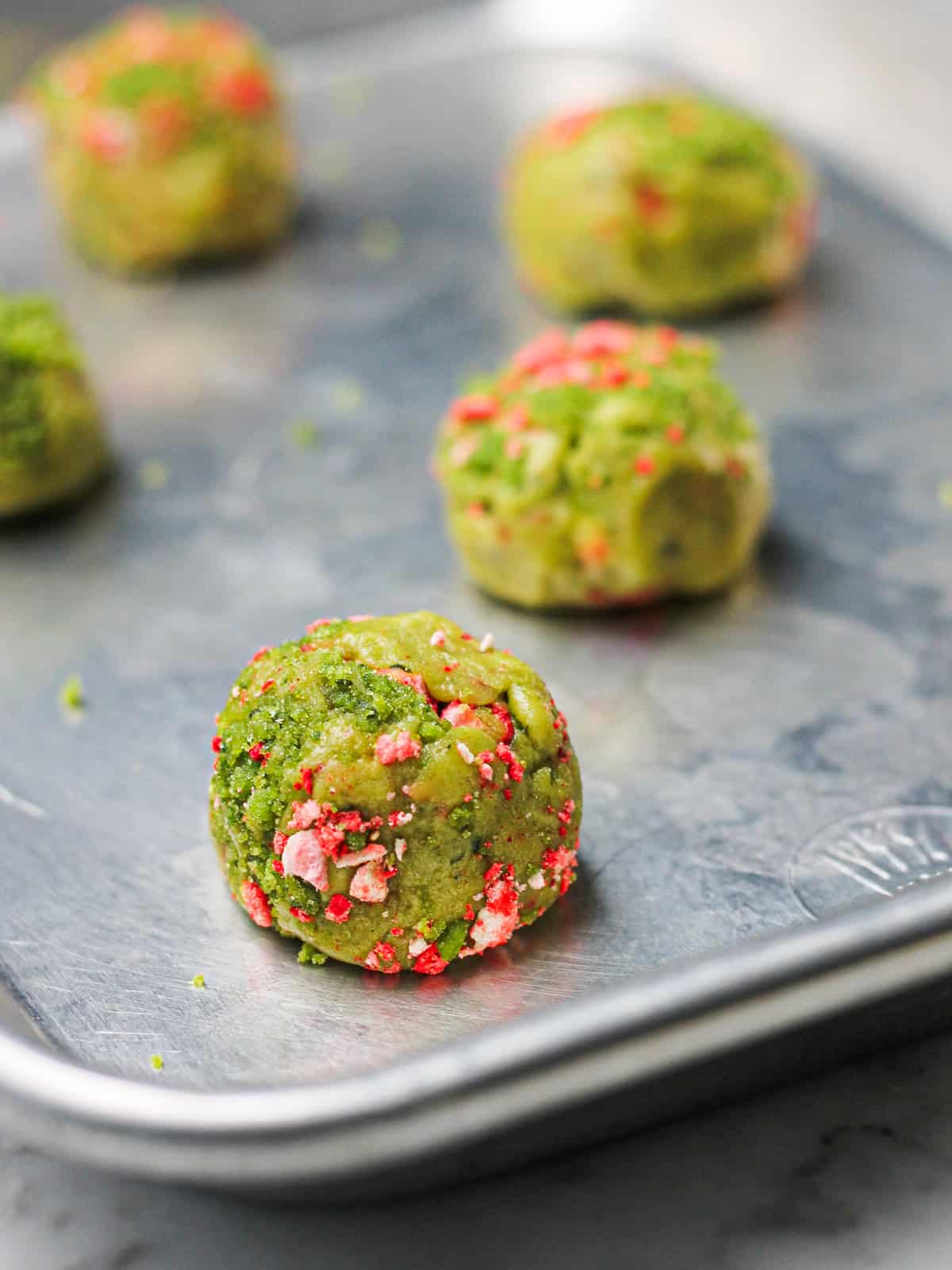 Strawberry basil sugar cookie dough balls on a baking sheet with strawberry pieces pressed on top.