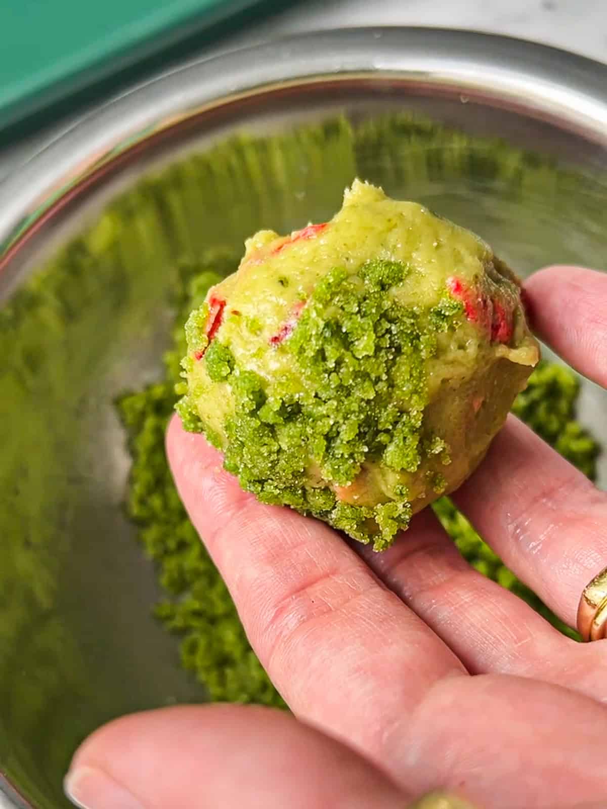 Hand holding a green dough ball rolled in basil sugar.