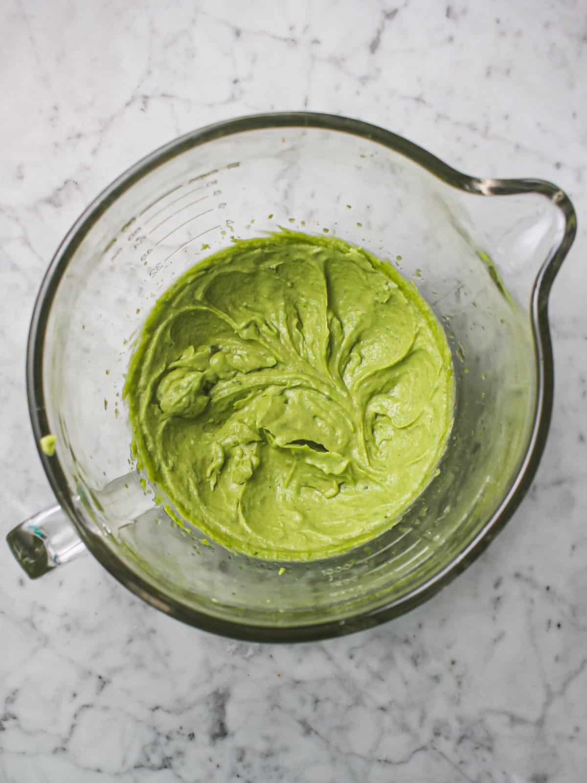 Basil sugar and butter combined in a clear mixing bowl to form green dough.