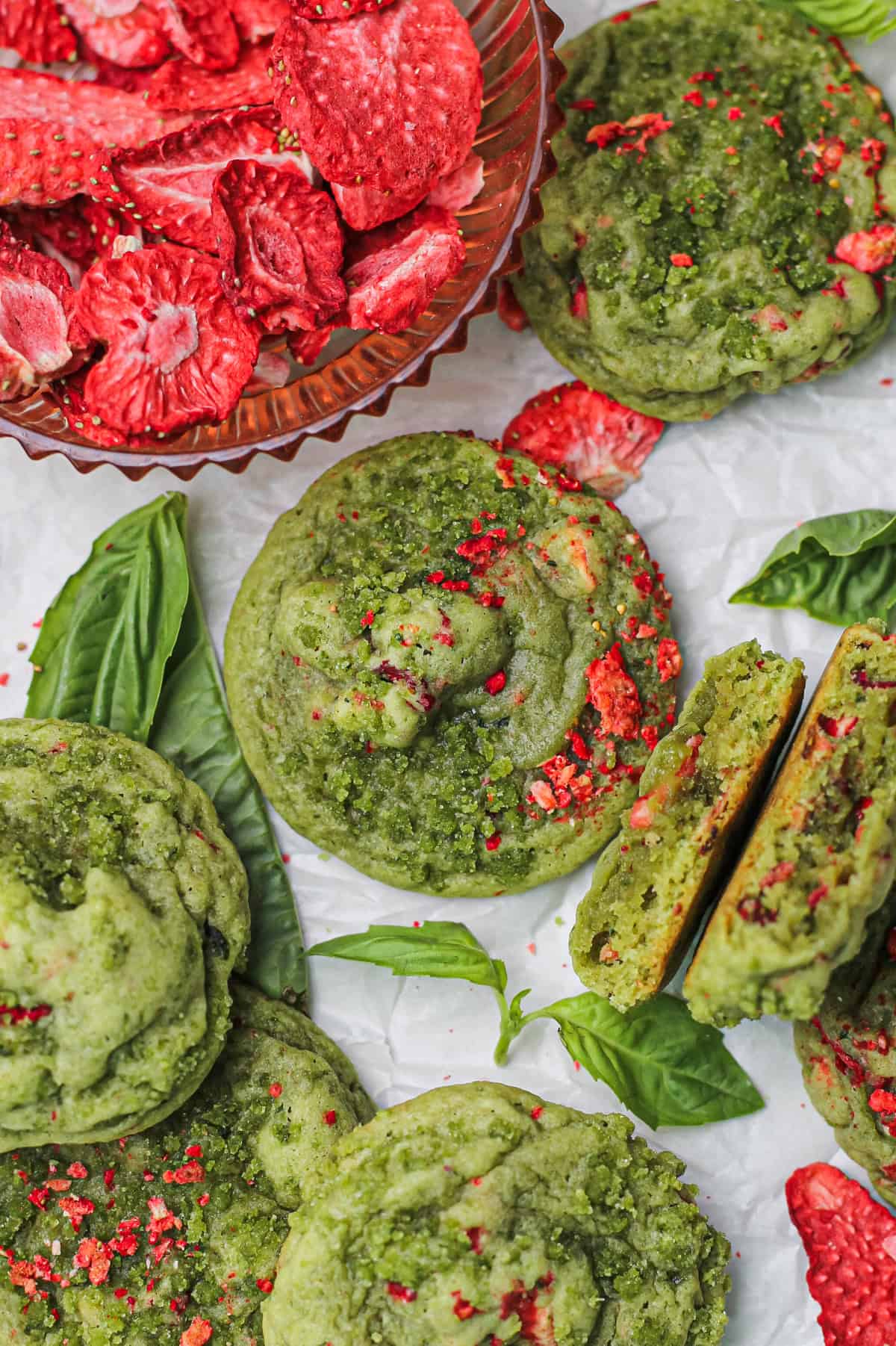 Soft strawberry basil sugar cookies with freeze-dried strawberry pieces pressed on top, on white parchment paper.