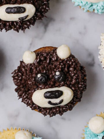 Overhead image of a teddy bear cupcake with brown fur, with white muzzle and ears, alongside black details for his face.