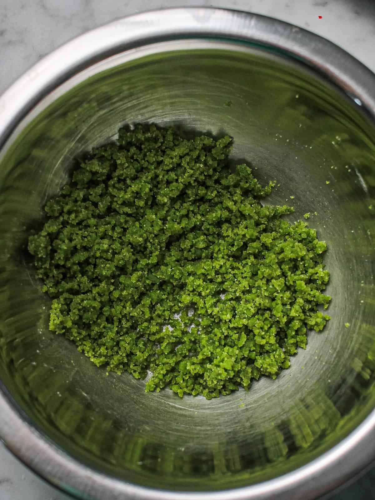 Green, sandy homemade basil sugar, made in a food processor and now in a metal mixing bowl.