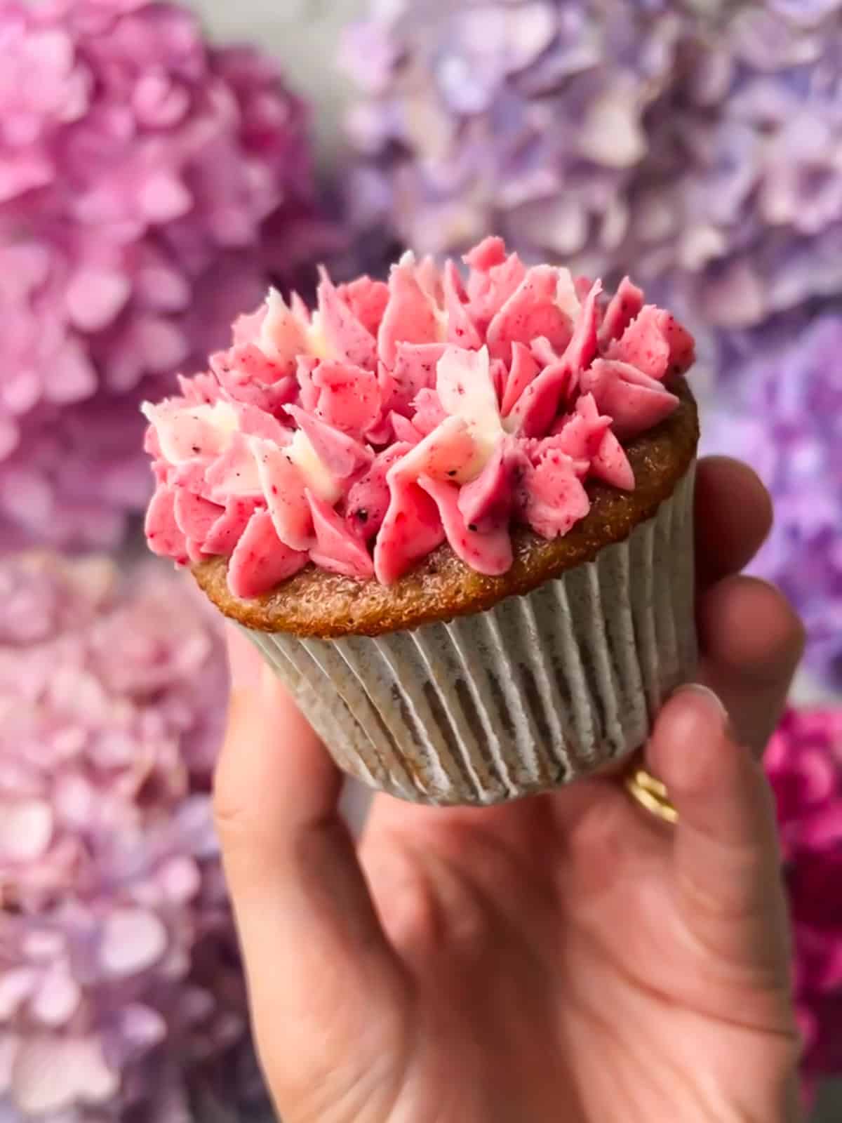Hand holding a finished, fully decorated hydrangea cupcake.