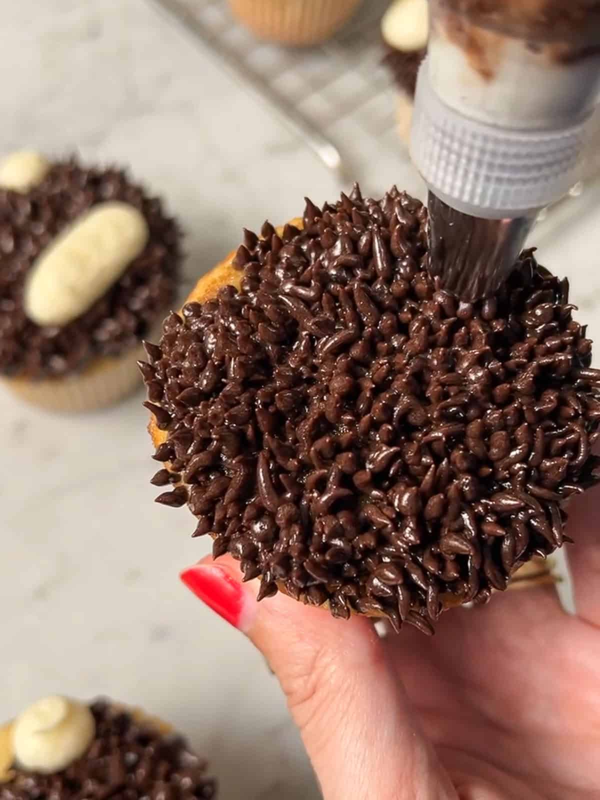 Piping chocolate buttercream fur onto a cupcake with a grass tip.