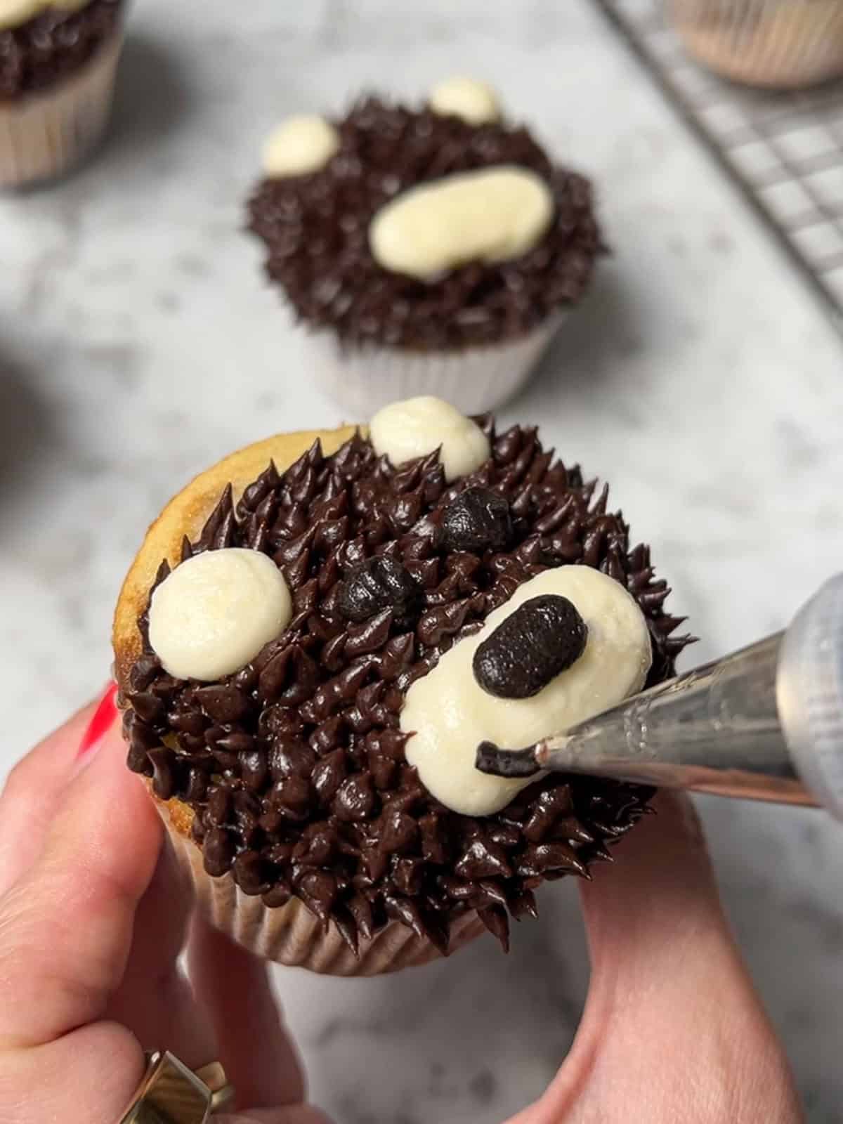 Piping a dark buttercream mouth onto a brown bear cupcake.
