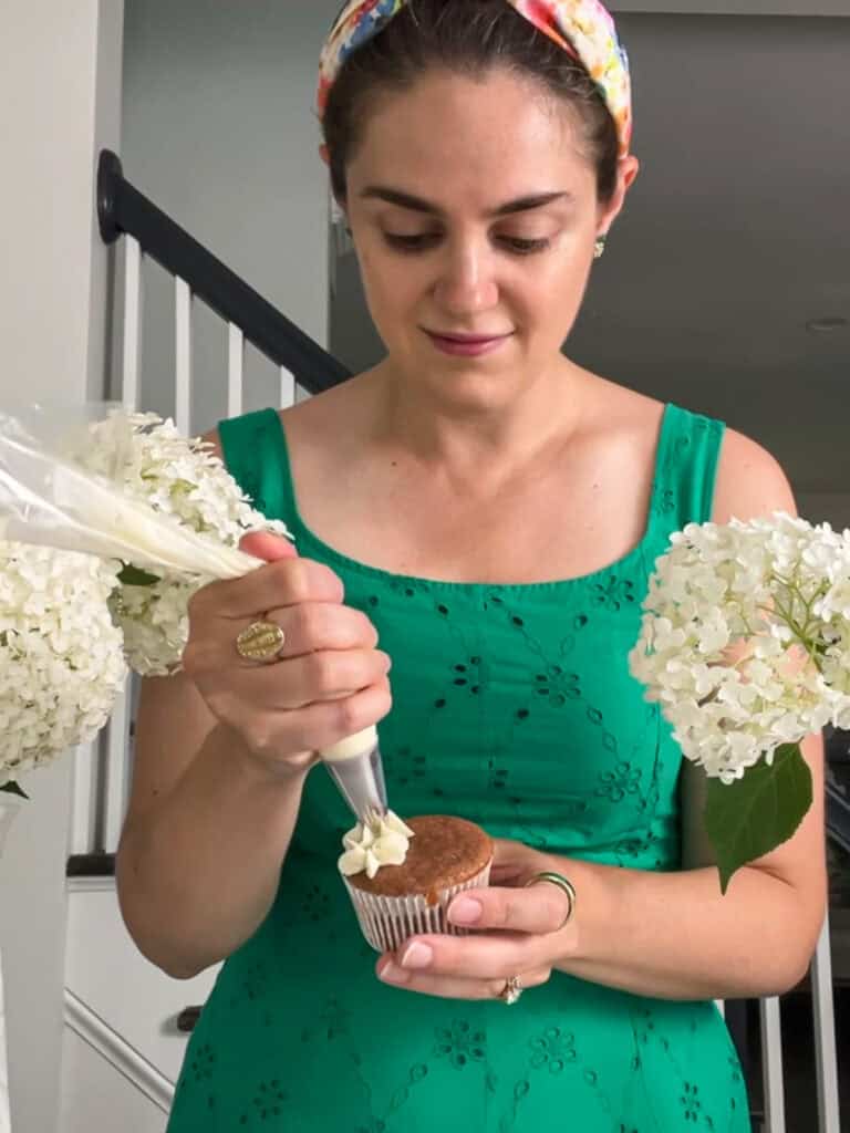 Susan piping white buttercream hydrangeas onto a cupcake.