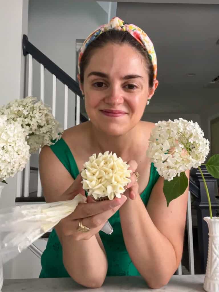 Susan holding a decorated cupcake that looks like a white hydrangea.