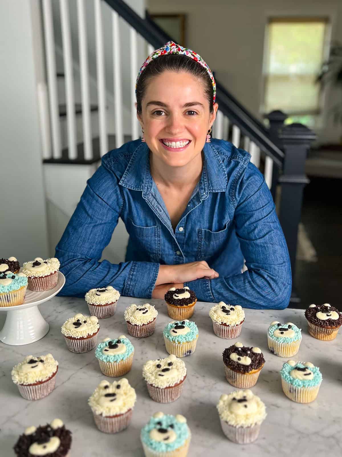 Susan standing behind a kitchen counter with assorted buttercream teddy bear cupcakes.