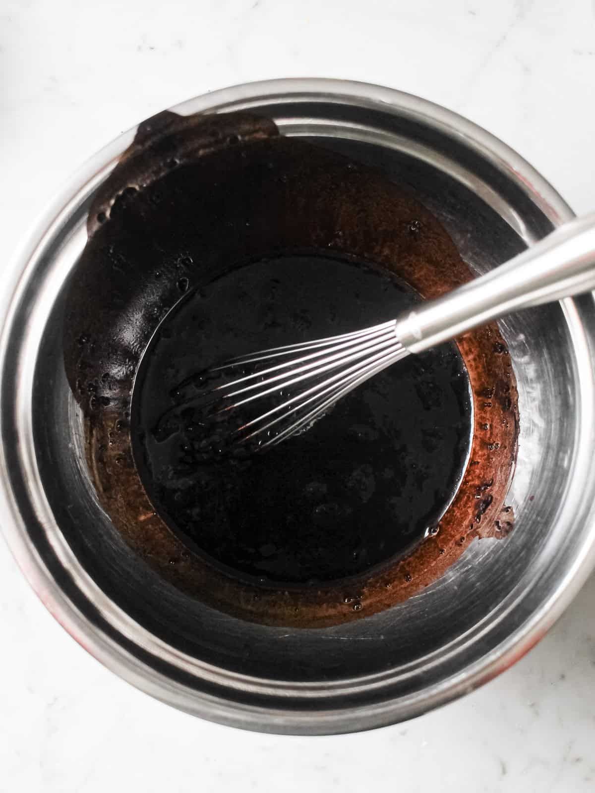 Dark black cocoa mixture in a mixing bowl with a whisk.