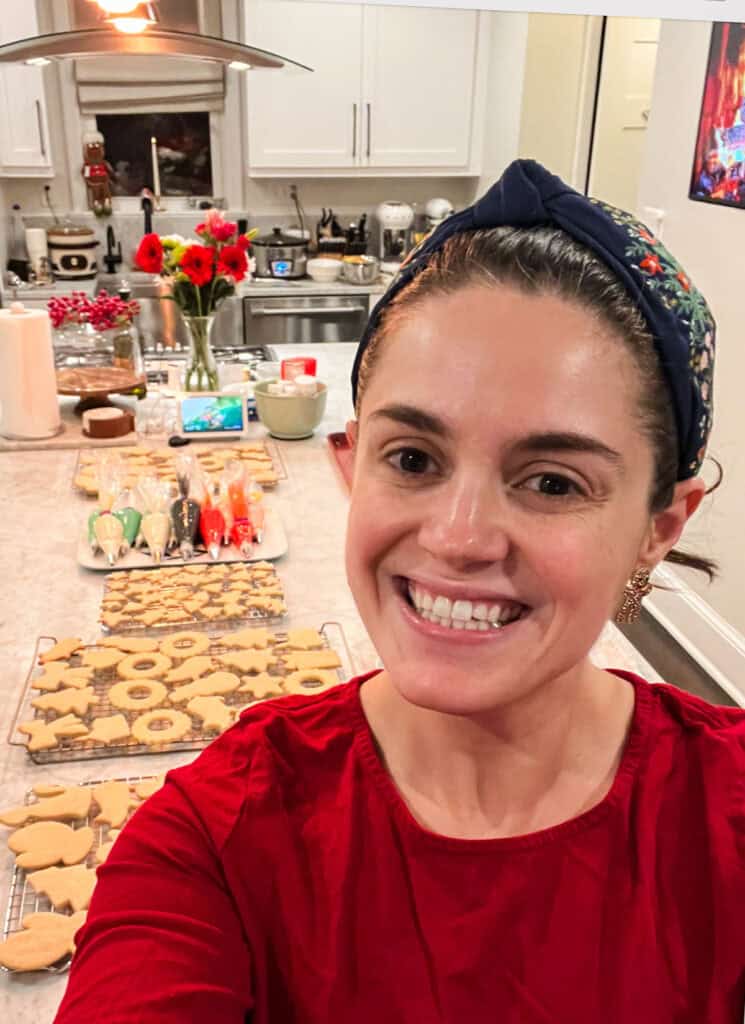 Selfie of Susan, with a kitchen counter filled with baked Christmas cookies, ready to be decorated at her annual cookie party.